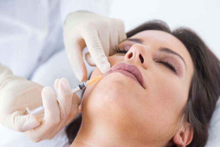 Beautiful young woman getting botox cosmetic injection in her fa