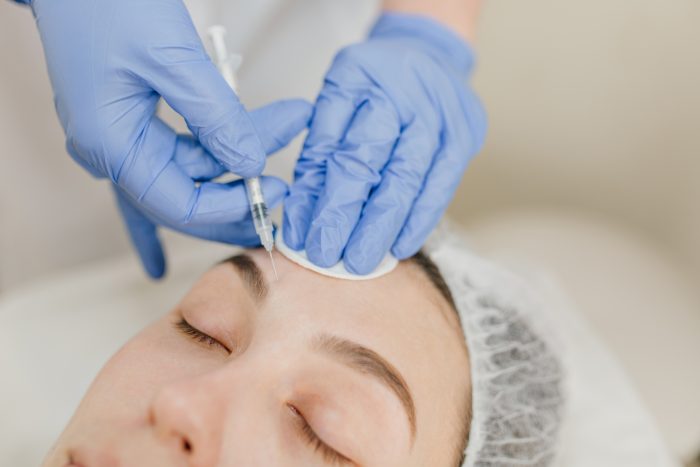 Closeup portrait hands in blue clinic gloves making injection on womans face. Rejuvenation, injecting, professional therapy, healthcare, plastic, botox, beauty.