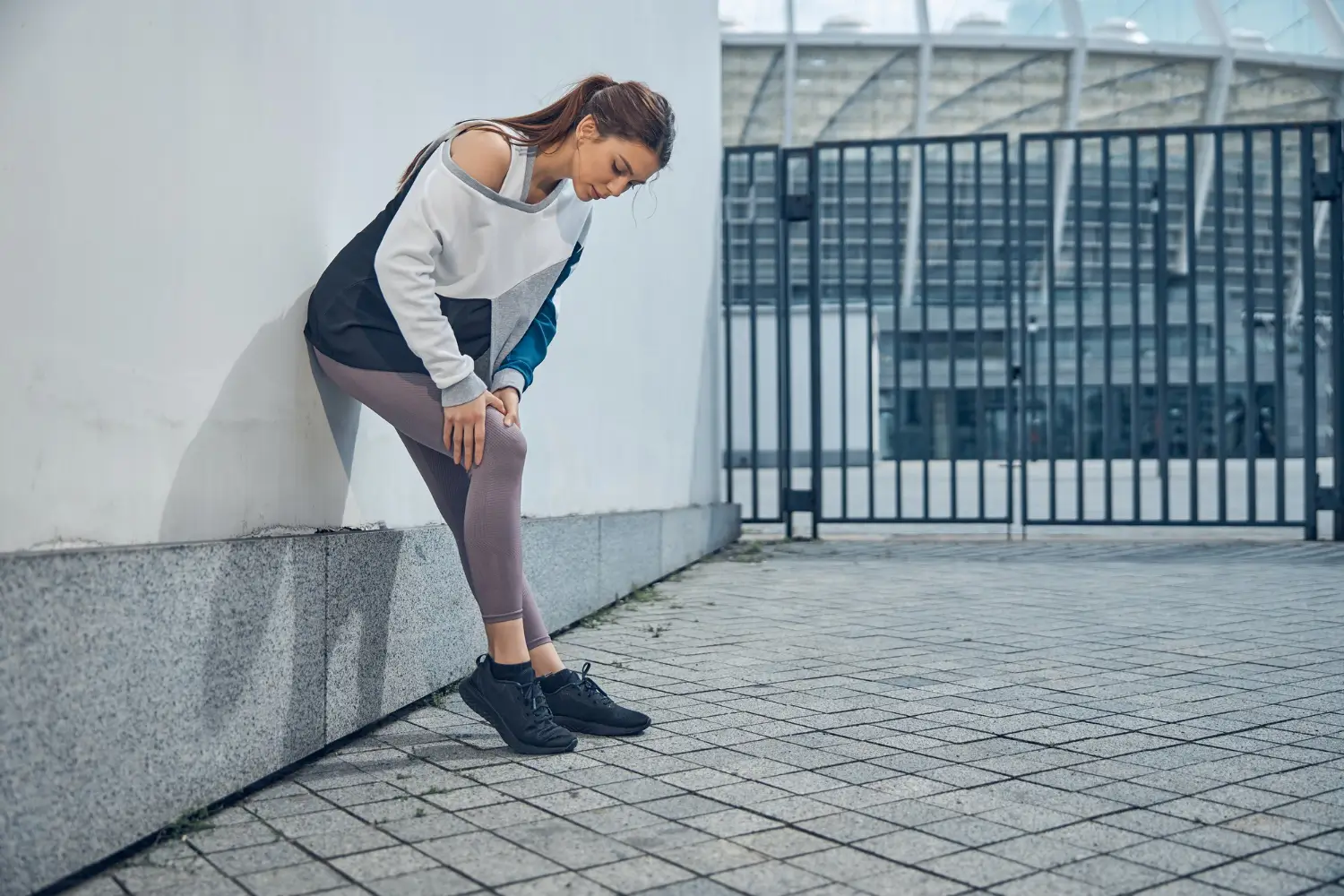 woman standing against the wall while checking her knee