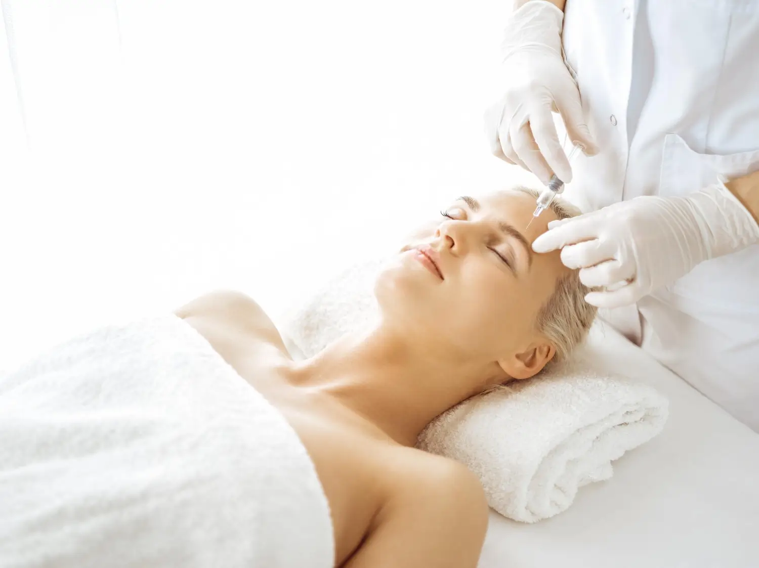 A female patient lying down in an aesthetic clinic receiving skin booster treatment.