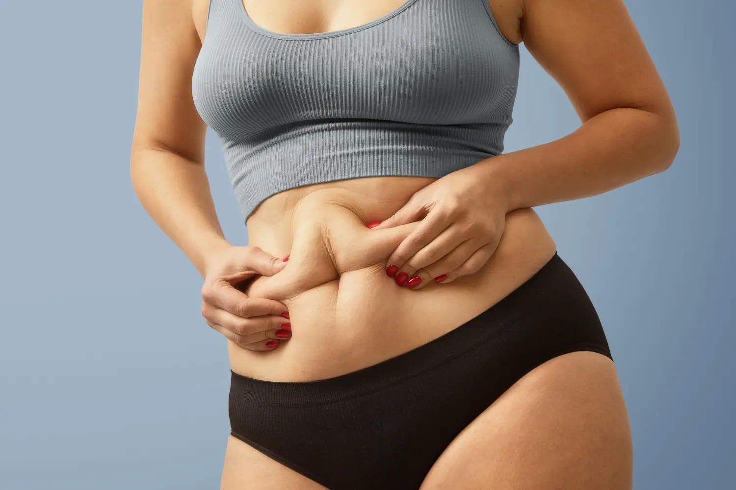 Woman pinches her belly fat, maybe considering non-surgical fat injection like Lemon Bottle or Aqualyx.