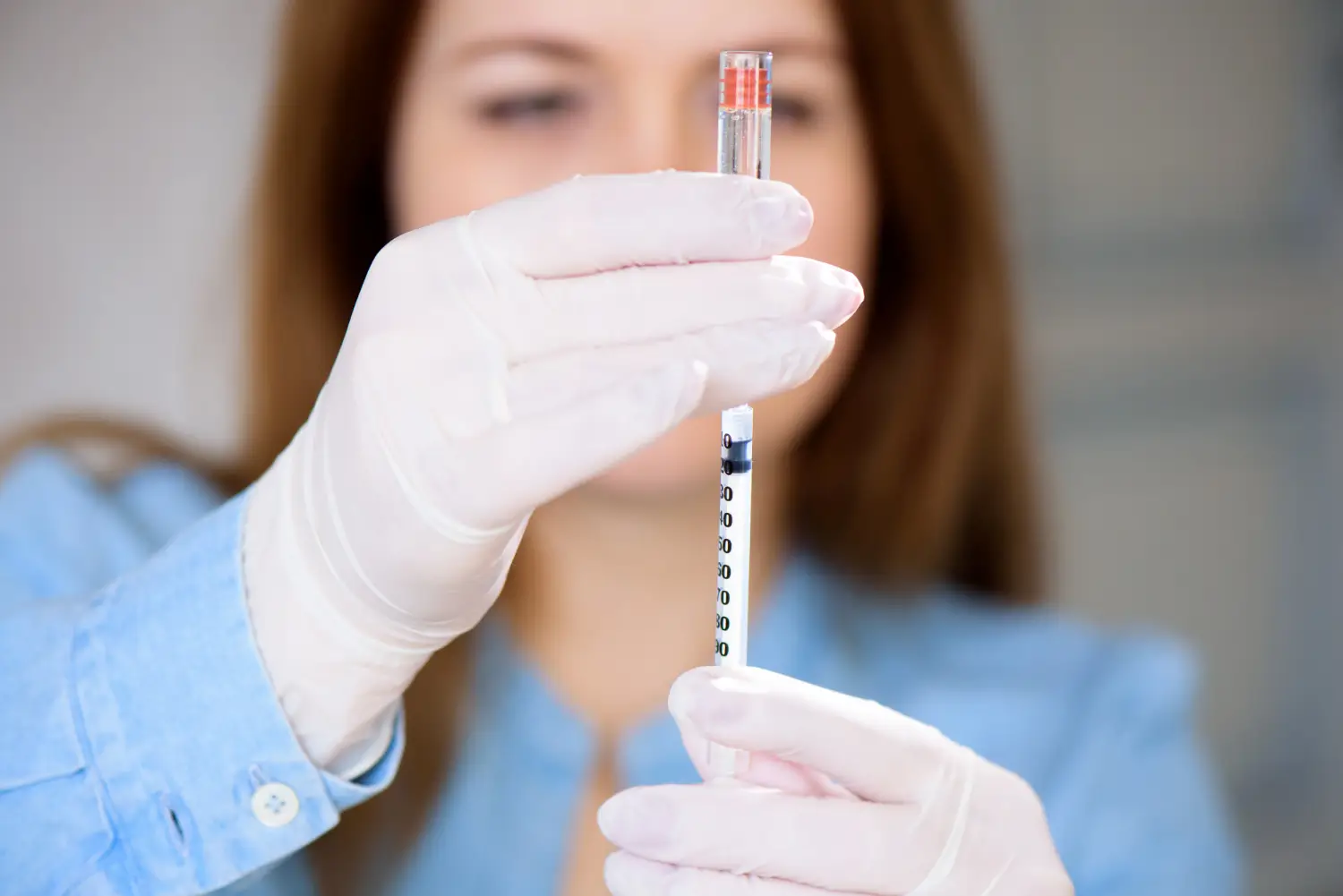 Nurse in gloves draws medication into a syringe from a vial for patient treatment.