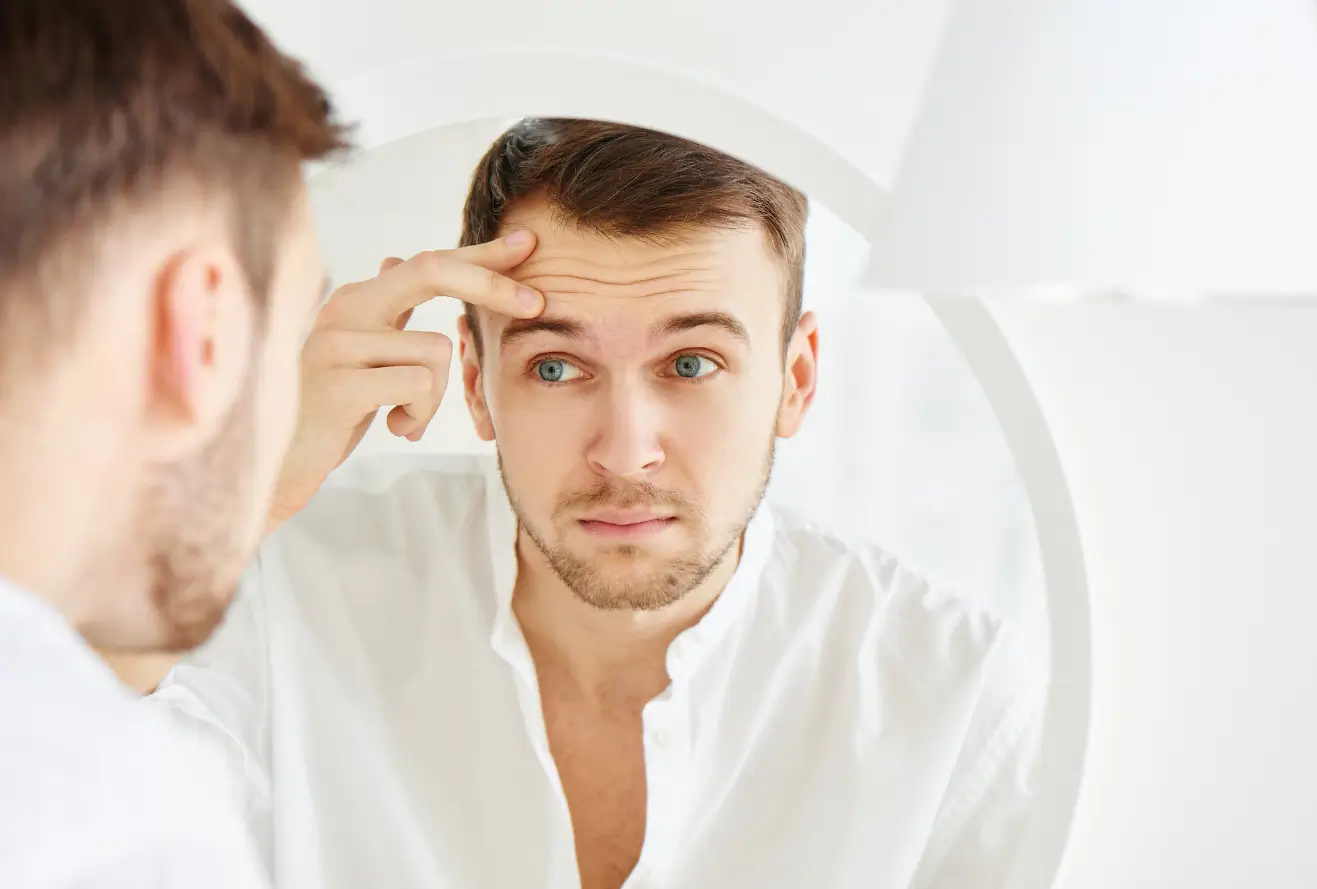 Male individual looking at his forehead wrinkles in the mirror.