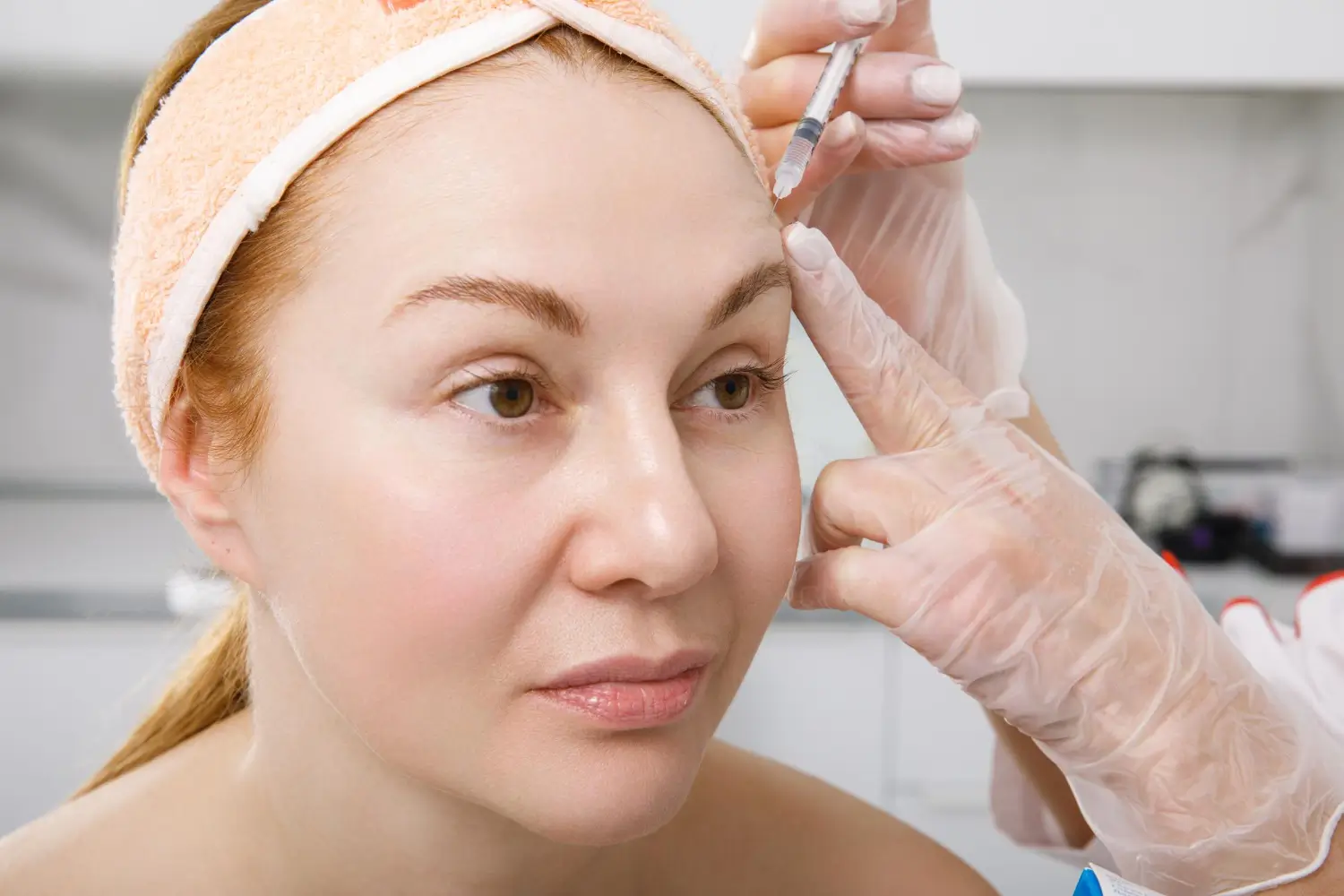 Medical professional performs an anti-wrinkle injection in the glabella area of a woman's forehead for a smoother appearance.